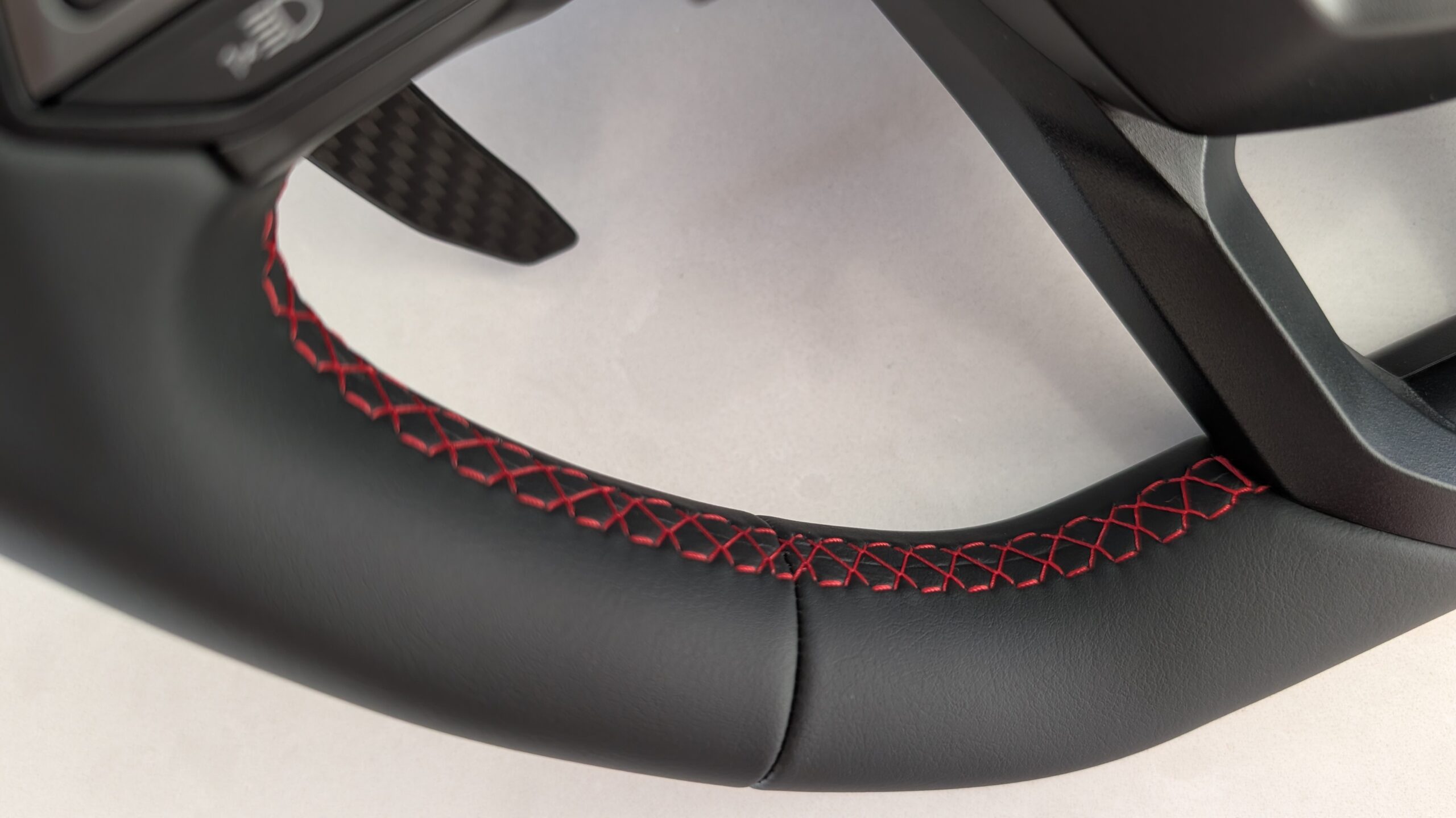 MOZA Lamborghini Revuelto rim close-up showing red cross-stitch detail on microfiber leather with carbon fibre shifter paddle visible