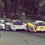 Three Group C prototypes cornering in Automobilista 2 - Mercedes-Sauber AEG, Toyota Eka/Motta, plus third car - tree-lined corner