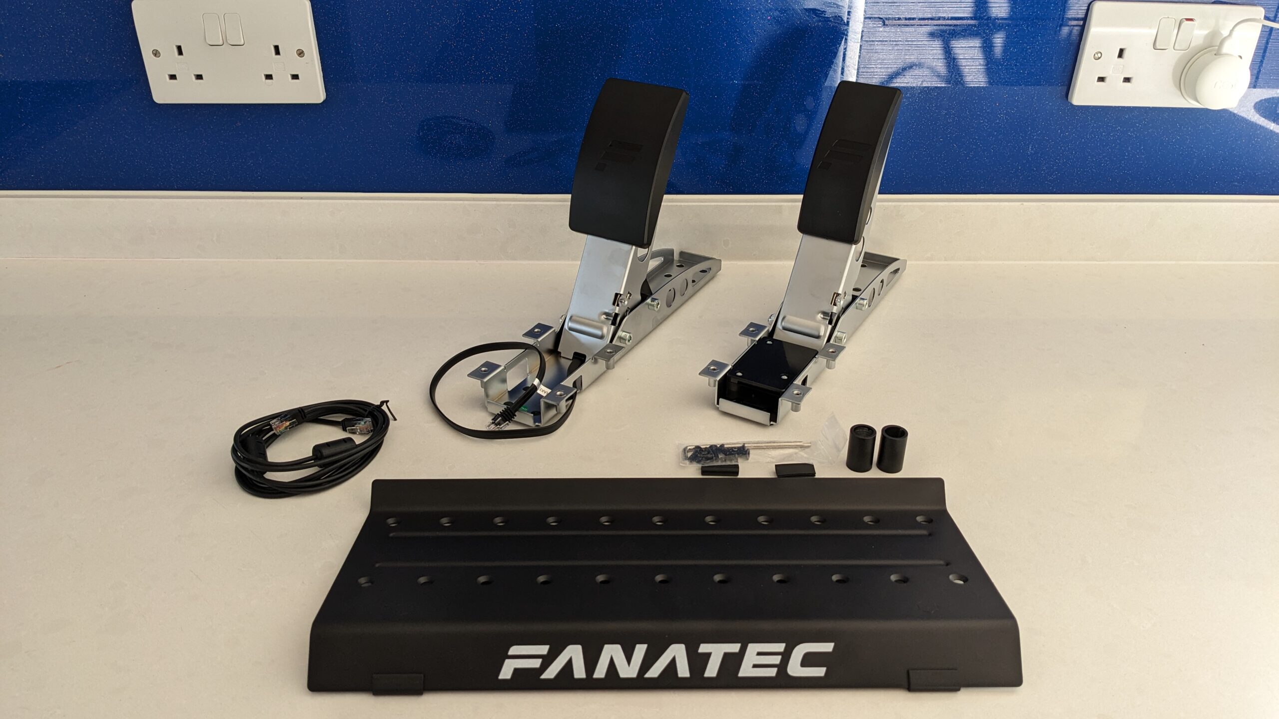 Sim racing load cell pedals laid out with the RJ12 connection cable and clip-on ferrite chokes
