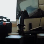 MOZA MH16 flight stick mounted on AB9 FFB base in foreground silhouette, secondary throttle quadrant in soft focus left, window light behind - atmospheric home flight sim setup