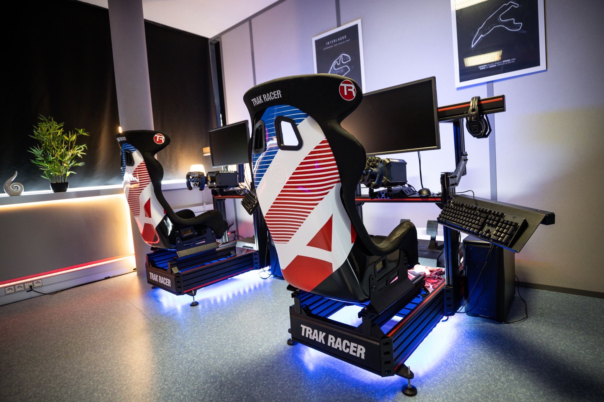 Two Trak Racer cockpits side by side under blue LED lighting, race-livery seats, monitors, Interlagos circuit map on the wall