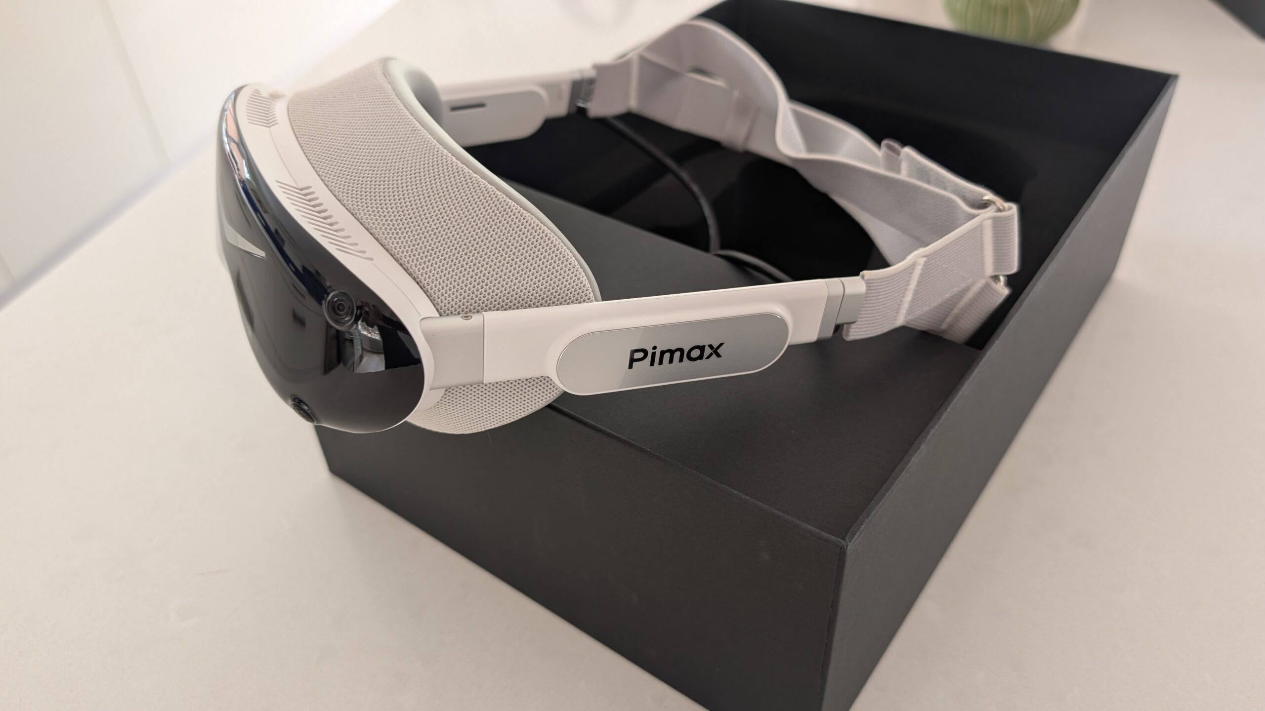 A white Pimax Dream Air SLAM with its grey fabric facial interface and white strap resting on its open black box