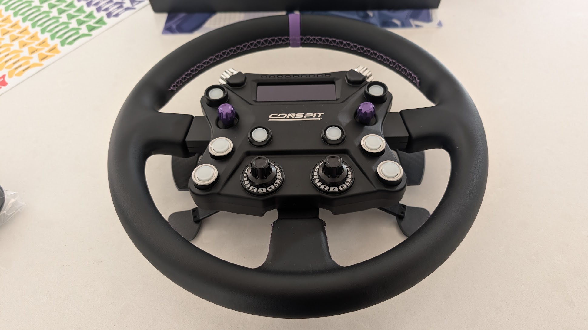 Conspit 310 APEX front view on a white worktop: purple centre marker, screen, LED row, buttons, joysticks and rotary switches