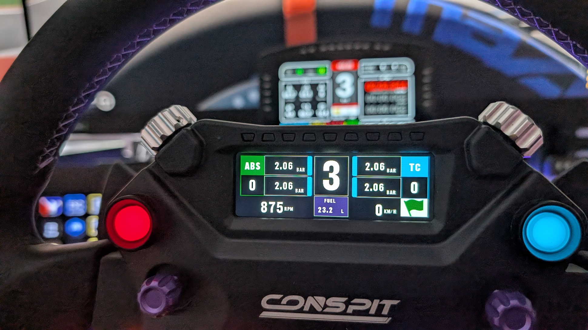 The 2.99-inch screen of the Conspit 310 APEX showing ABS and TC, 3rd gear, rpm and fuel, with the Grid DDU behind