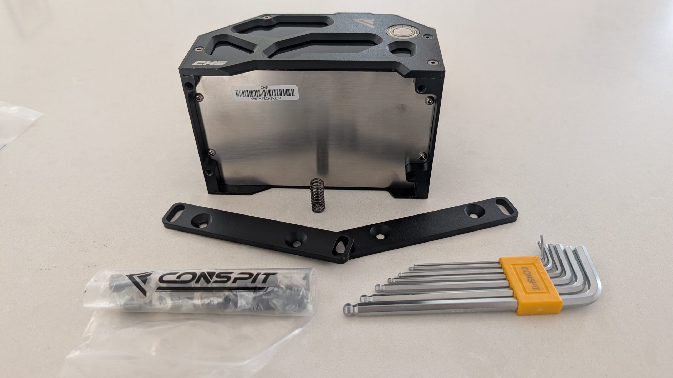 Underside of the CONSPIT CHS with serial sticker, the two brackets, Allen keys, bolt bag and the loose spring on a worktop