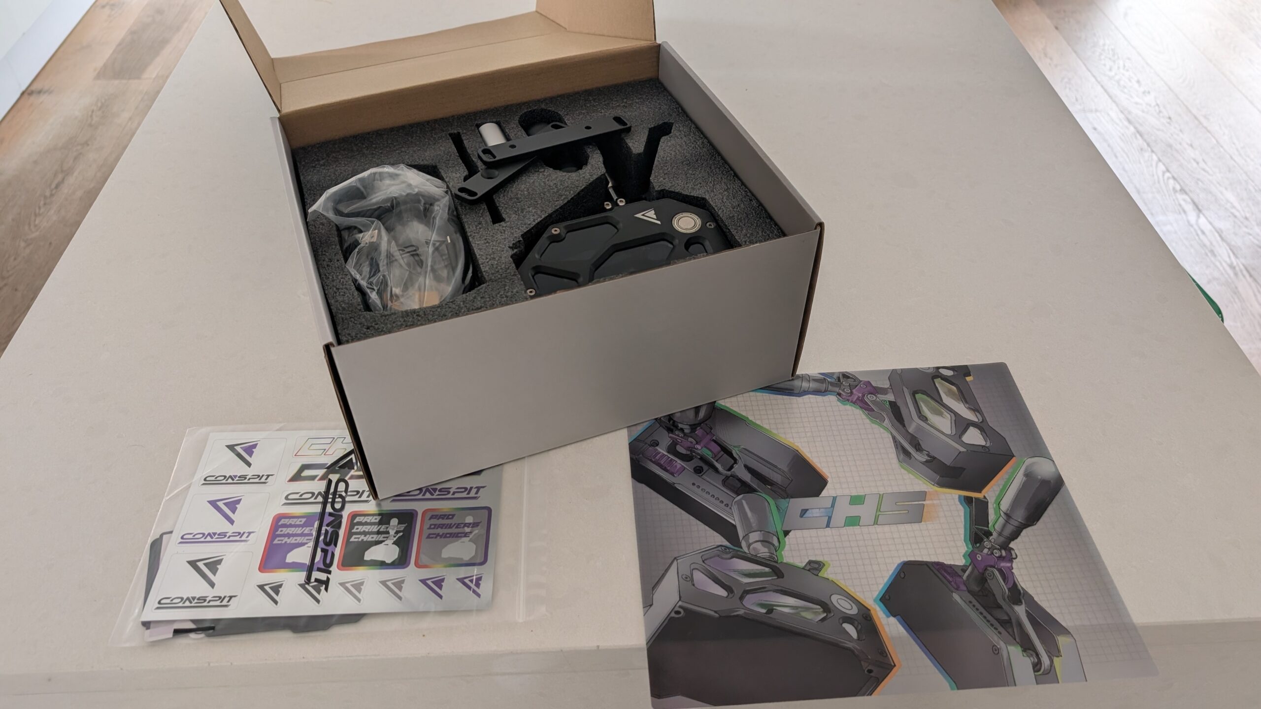 CONSPIT CHS box open showing the shifter in foam, the sticker sheet and the illustrated clear art sheet