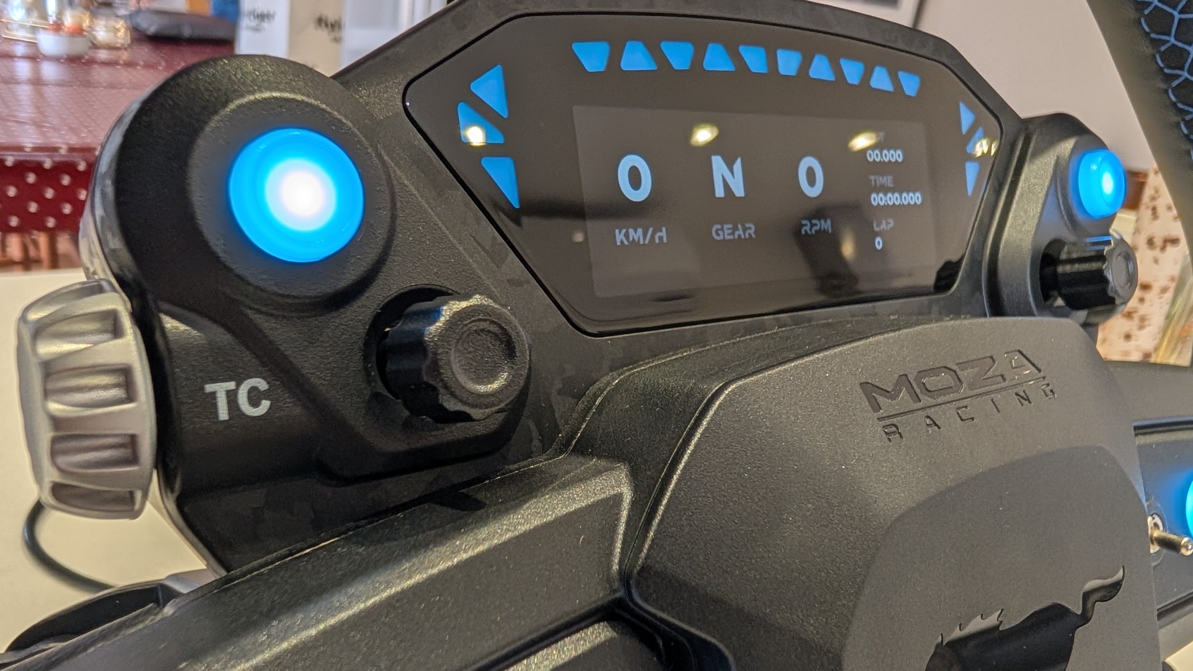 Angled close-up of the MOZA Mustang GTD wheel display, the TC label and a silver thumb wheel