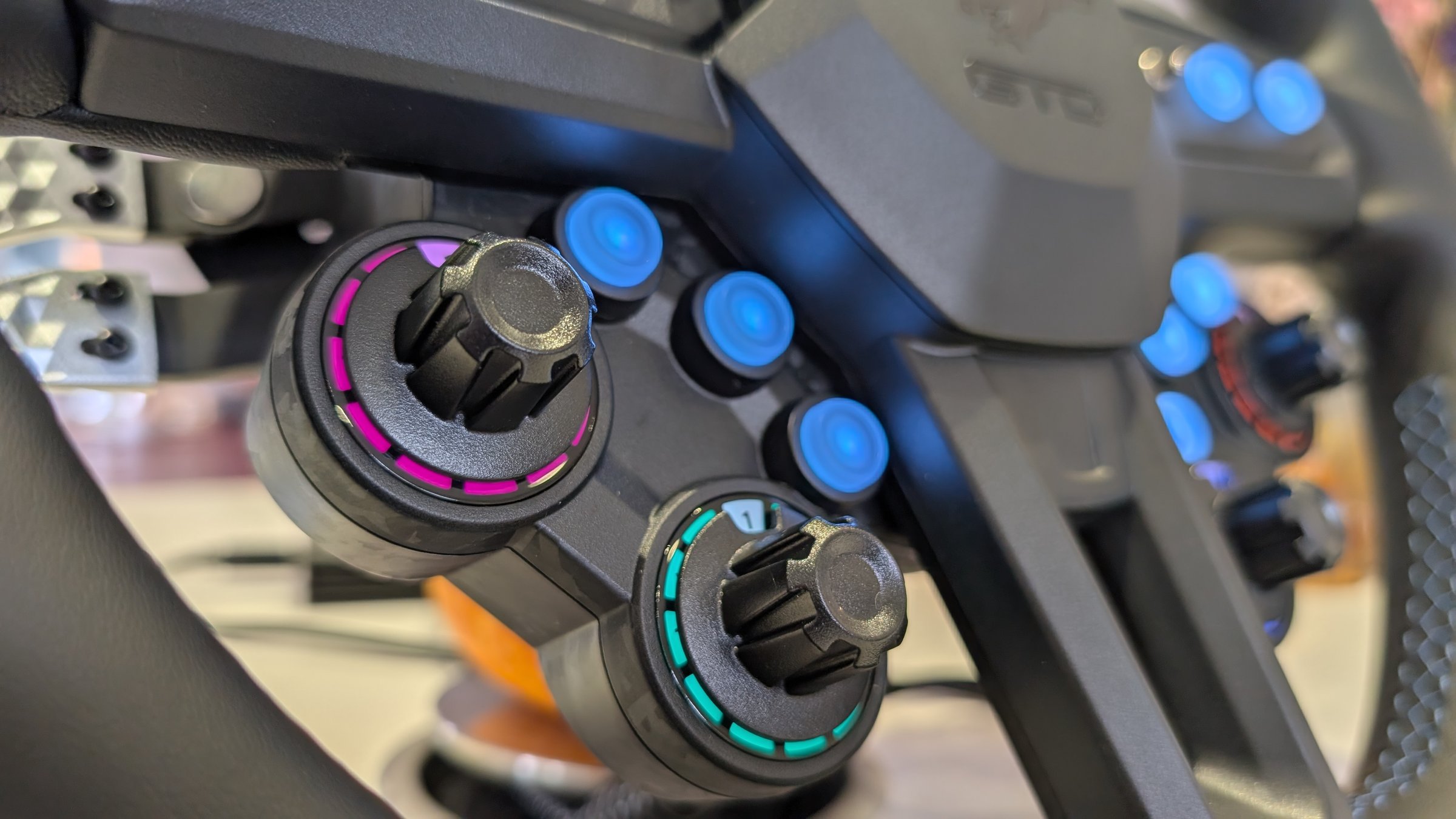 Close-up of two MOZA Mustang GTD rotary encoders with knurled black caps and magenta and teal LED rings